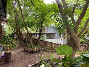 Un jardín con diversas plantas y árboles, una valla de bambú y un edificio con tejado de tejas.