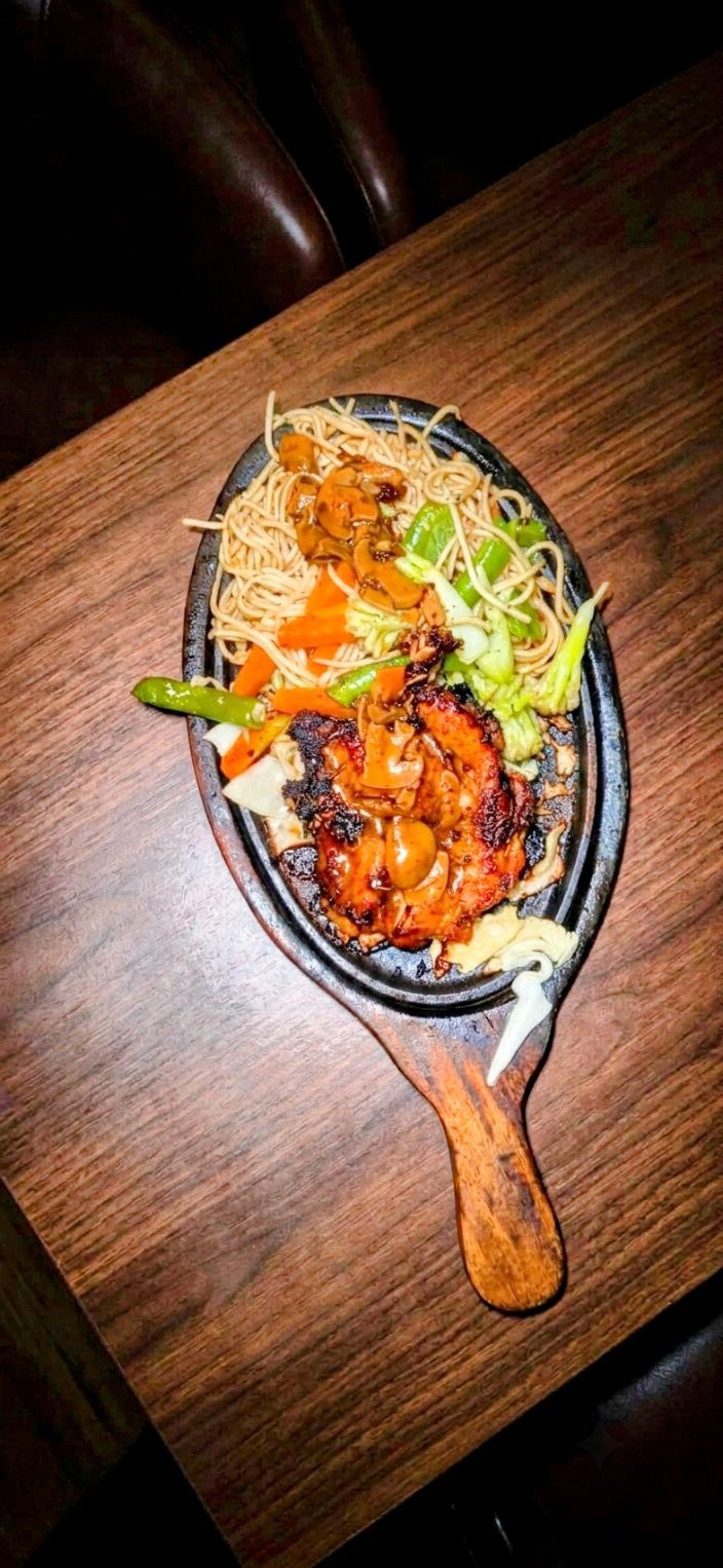 A meal served on a black plate with a wooden handle, placed on a wooden table.