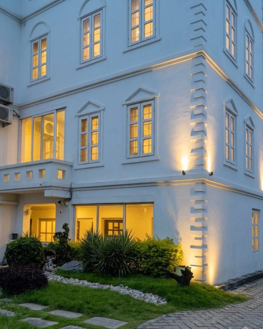 Ein mehrstöckiges Gebäude mit beleuchteten Fenstern und einem gepflegten Garten.