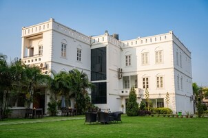 Un edificio blanco con varias ventanas y balcones, rodeado por un césped cuidado y palmeras.