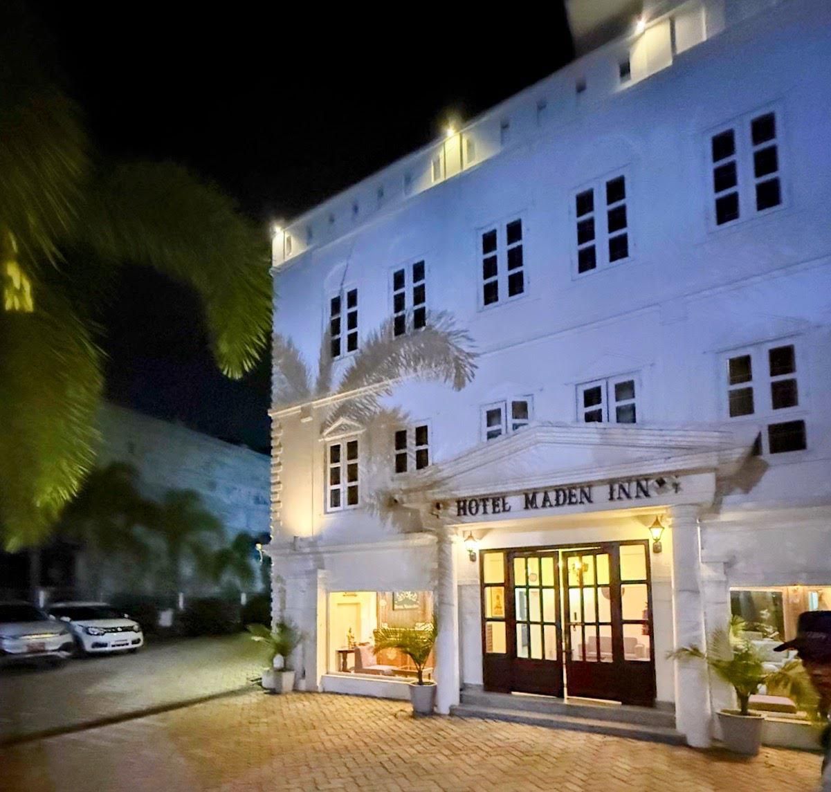 Un edificio blanco con un cartel que dice 'HOTEL MADEN INN' en la entrada.