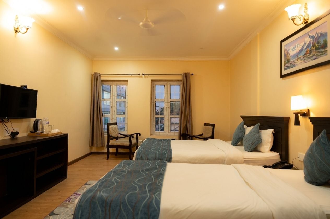 A hotel room with two beds, a television, a desk, and a chair.