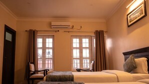 Habitación de hotel con dos camas, una silla, un ventanal con cortinas, un equipo de aire acondicionado y un cuadro en la pared.