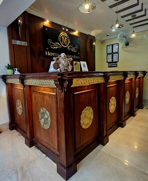 Una mesa de recepción con un letrero que indica Golden Inn, un área de recepción con detalles de madera e iluminación empotrada en el techo.