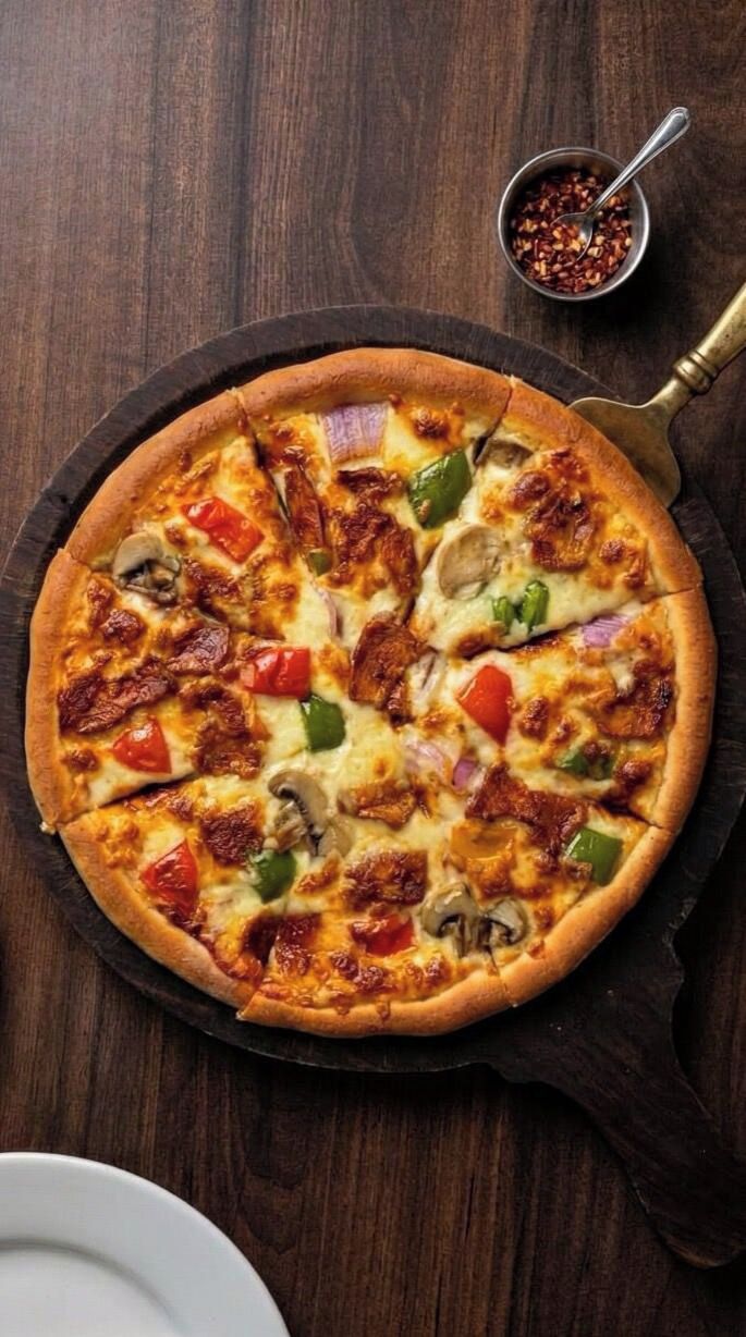 Une pizza sur un plat rond noir, avec une table en bois rustique en arrière-plan.