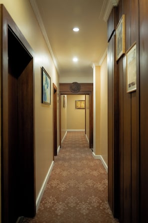 A hotel hallway with wooden doors, framed artwork on the walls, and a patterned carpet.