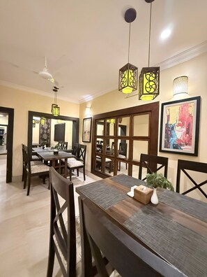 A dining area with a wooden table, chairs, pendant lights, and framed artwork on the walls.