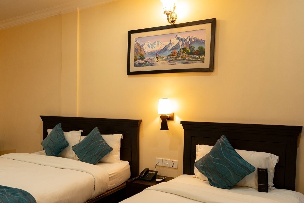 Habitación de hotel con dos camas, un cuadro en la pared, una lámpara de noche y un teléfono en la mesita.