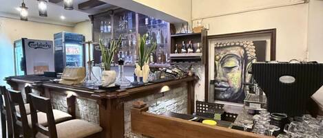 A bar area with wooden bar stools, a chandelier, and a large painting on the wall.