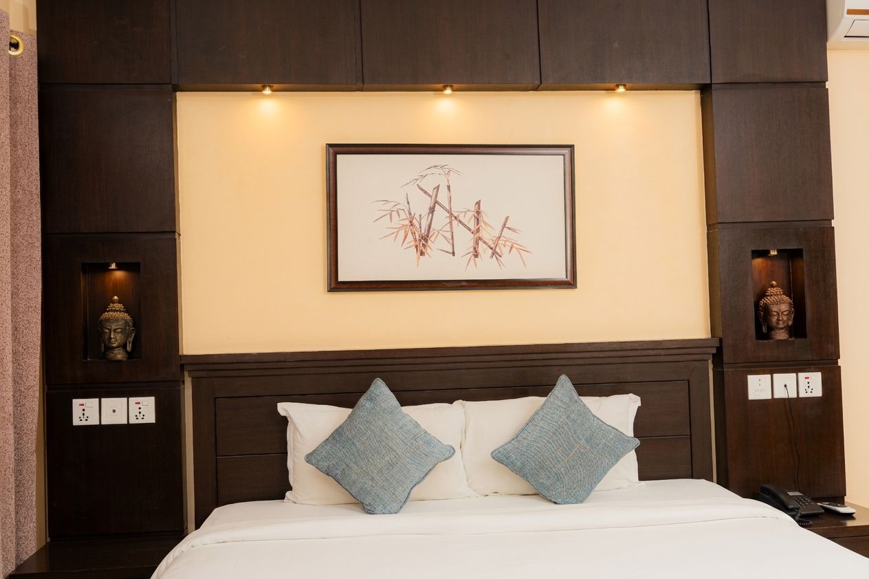 Una habitación de hotel con cama, dos almohadas, una obra de arte enmarcada y una estatua de Buda en la pared.