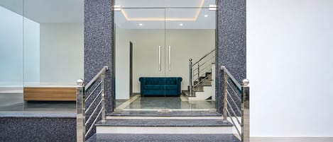 Un intérieur moderne avec un escalier menant à un espace de vie, comprenant un canapé turquoise et une cloison en verre.