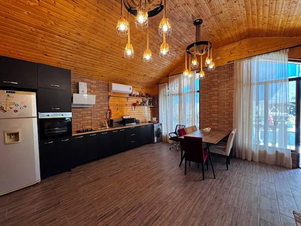A modern kitchen with wooden ceiling, built-in appliances, and a dining area with a table and chairs.