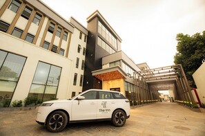 A white car parked in front of a building with a modern design, featuring a large glass entrance and a wooden canopy.