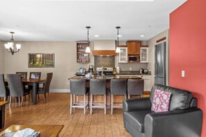 Una cocina moderna con taburetes de bar, un comedor con mesa y sillas, y una sala de estar con sofá.