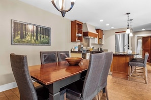 Un comedor con mesa y sillas de madera, una cocina con armarios de madera y un gran cuadro de un bosque enmarcado en la pared.