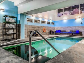 Una piscina con fondo de cristal, un área de descanso con cojines azules y un estante con toallas dobladas.