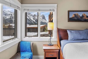 A hotel room with a bed, a nightstand, a lamp, a chair, and a window with a mountain view. - The ‘106’ by Fern James
Adventure Awaits! (Canmore)