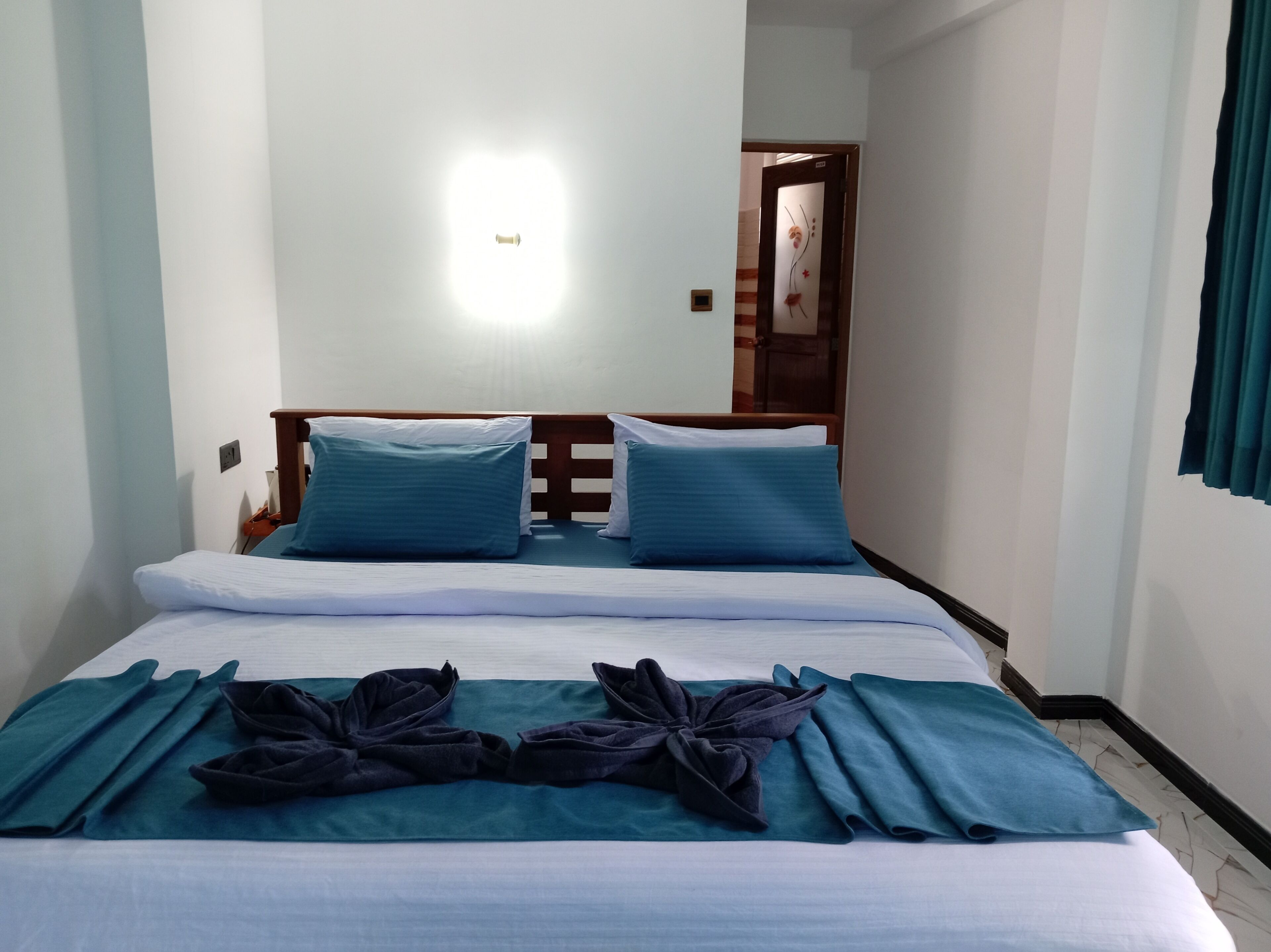 Een hotelkamer met een bed, twee kussens, een net opgemaakt beddegoed en een handdoekstapel op de vloer.