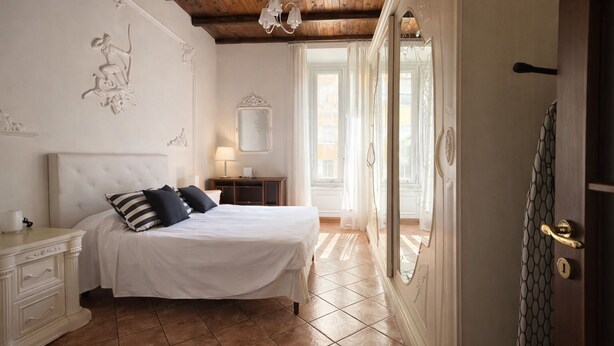 A bedroom with a large bed, a nightstand, a dresser, a mirror, and a door with a patterned curtain. - BORGO APARTMENT IMPERO VATICANO (Roma)