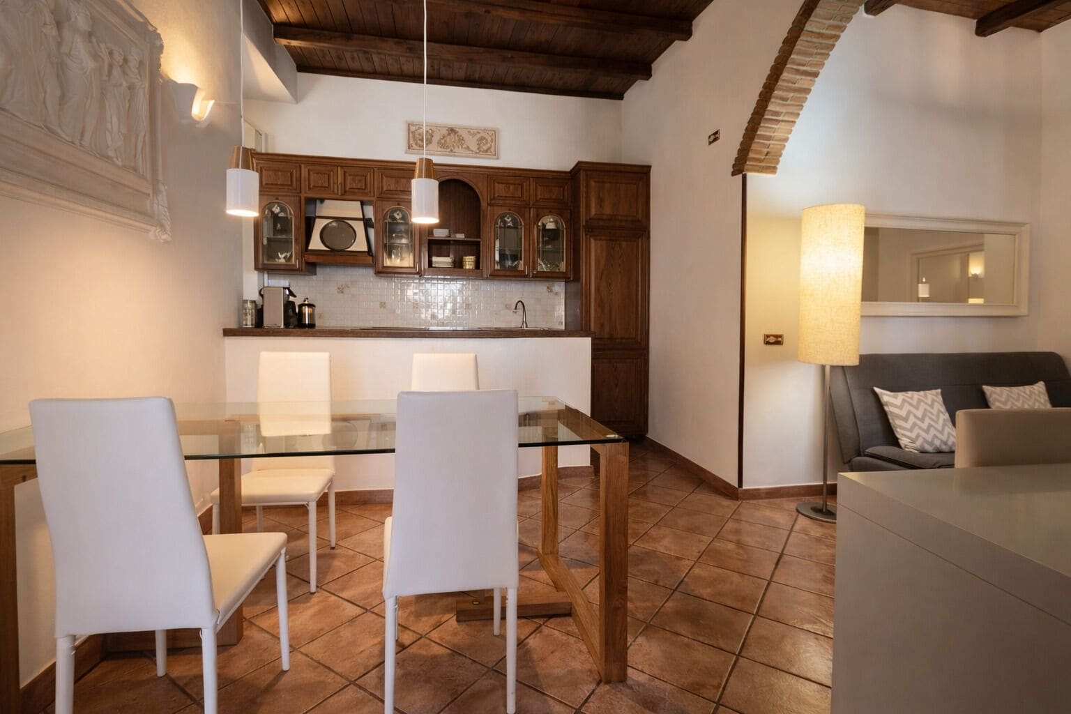A dining area with a glass table and white chairs, wooden cabinets, and a tiled floor.