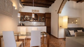 A dining area with a glass table and white chairs, wooden cabinets, and a tiled floor. - BORGO APARTMENT IMPERO VATICANO (Roma)