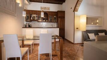 A dining area with a glass table and white chairs, wooden cabinets, and a tiled floor.
