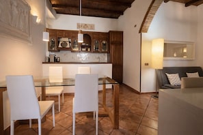 A dining area with a glass table and white chairs, wooden cabinets, and a tiled floor. - BORGO APARTMENT IMPERO VATICANO (Roma)