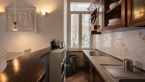 A kitchen with a dark countertop, a window with decorative glass, and wooden cabinets. - BORGO APARTMENT IMPERO VATICANO (Roma)