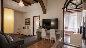 A living room with a sofa, a glass coffee table, a TV, and a desk with chairs. - BORGO APARTMENT IMPERO VATICANO (Roma)