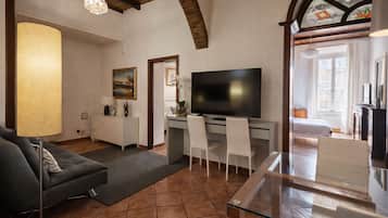 A living room with a sofa, a glass coffee table, a TV, and a desk with chairs.