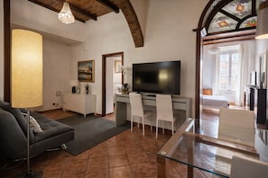 A living room with a sofa, a glass coffee table, a TV, and a desk with chairs. - BORGO APARTMENT IMPERO VATICANO (Roma)