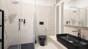 A modern bathroom with a glass-enclosed shower, a black sink, and a mirror above the sink.