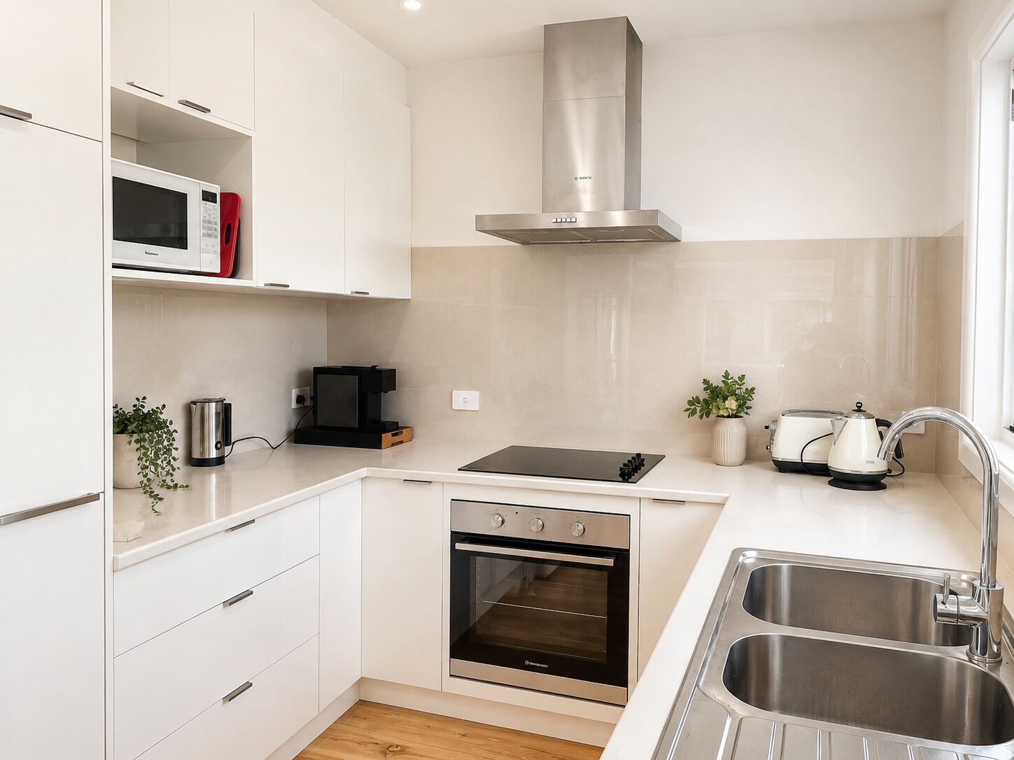 A modern kitchen with white cabinetry, a stainless steel range hood, a built-in oven, a microwave, and a sink.
