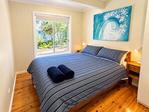 A bedroom with a large bed, two bedside lamps, a window with a view of greenery, and a painting on the wall. - Wirani on the Water (Sanctuary Point)