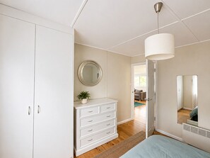 Ein Schlafzimmer mit einem Bett, einem Schminktisch, einem Spiegel und einer Tür zu einem weiteren Raum.
