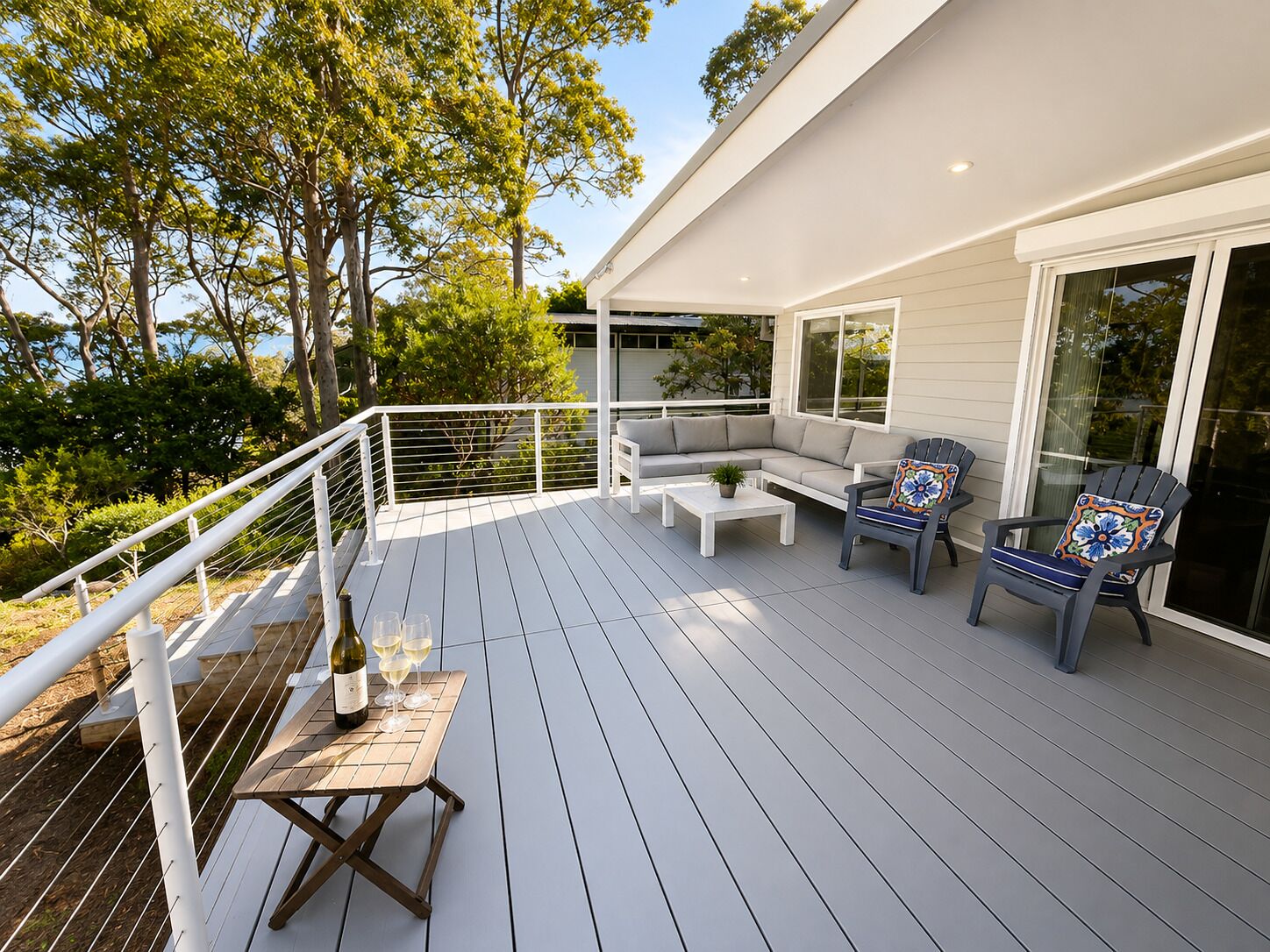 A deck with a sofa, chairs, and a table with glasses and a bottle.