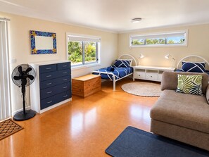 A bedroom with a bed, bedside tables, a dresser, a fan, and a window with a view of greenery. - Wirani on the Water (Sanctuary Point)