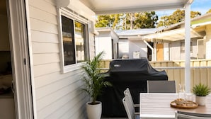 Eine überdachte Terrasse im Freien mit Esstisch und Stühlen, einem Grill und einem Blumentopf.