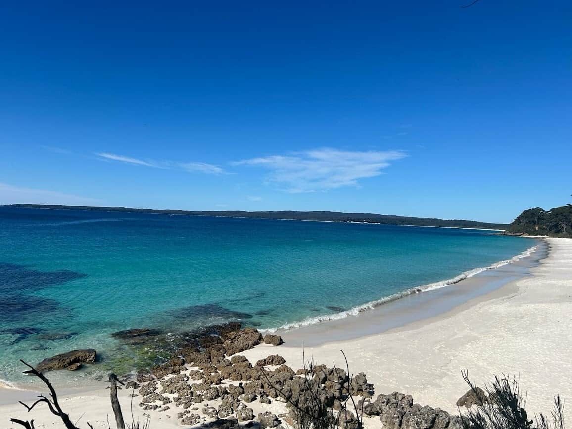 A beach with clear turquoise water, a sandy shore, and rocky outcrops.