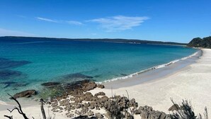 Ein Strand mit klarem türkisblauem Wasser, Sand und Felsformationen.