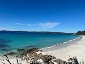 Ein Strand mit klarem türkisblauem Wasser, Sand und Felsformationen.