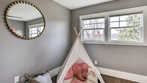 A room with a grey wall, a white ceiling, a large mirror, a window with a view of trees, and a teepee with a rainbow pillow. - Family Home, Hot Tub, Near Whiskey Row (Prescott)
