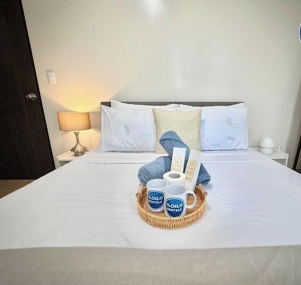 A neatly made bed with a basket of toiletries, a pair of slippers, and a book on a hotel room.