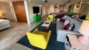 A hotel room with a bed, a sofa, a yellow armchair, a dining area with a table and chairs, a kitchen area, and a ceiling fan. - Oceanview 2BR/2BA condo with pool, AC, balcony, and beach access-Kanai A Nalu 317 (Wailuku)