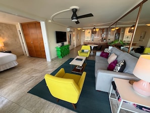A hotel room with a bed, a sofa, a yellow armchair, a dining area with a table and chairs, a kitchen area, and a ceiling fan. - Oceanview 2BR/2BA condo with pool, AC, balcony, and beach access-Kanai A Nalu 317 (Wailuku)