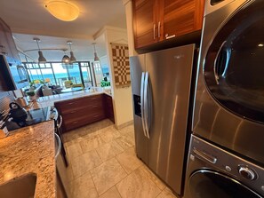 A modern kitchen with a stainless steel refrigerator, wooden cabinets, and a view to the outside. - Oceanview 2BR/2BA condo with pool, AC, balcony, and beach access-Kanai A Nalu 317 (Wailuku)