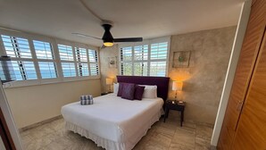 A bedroom with a large bed, a ceiling fan, a nightstand, and a window with blinds. - Oceanview 2BR/2BA condo with pool, AC, balcony, and beach access-Kanai A Nalu 317 (Wailuku)