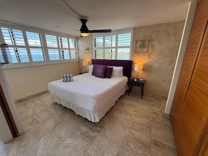 A bedroom with a large bed, a ceiling fan, a nightstand, and a window with blinds. - Oceanview 2BR/2BA condo with pool, AC, balcony, and beach access-Kanai A Nalu 317 (Wailuku)