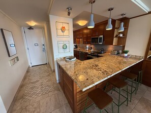 A modern kitchen with granite countertops, stainless steel appliances, and pendant lighting. - Oceanview 2BR/2BA condo with pool, AC, balcony, and beach access-Kanai A Nalu 317 (Wailuku)