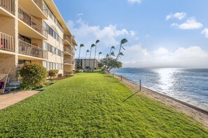A beachfront hotel with a well-maintained lawn, a view of the ocean, and a building with multiple balconies. - Oceanview 2BR/2BA condo with pool, AC, balcony, and beach access-Kanai A Nalu 317 (Wailuku)
